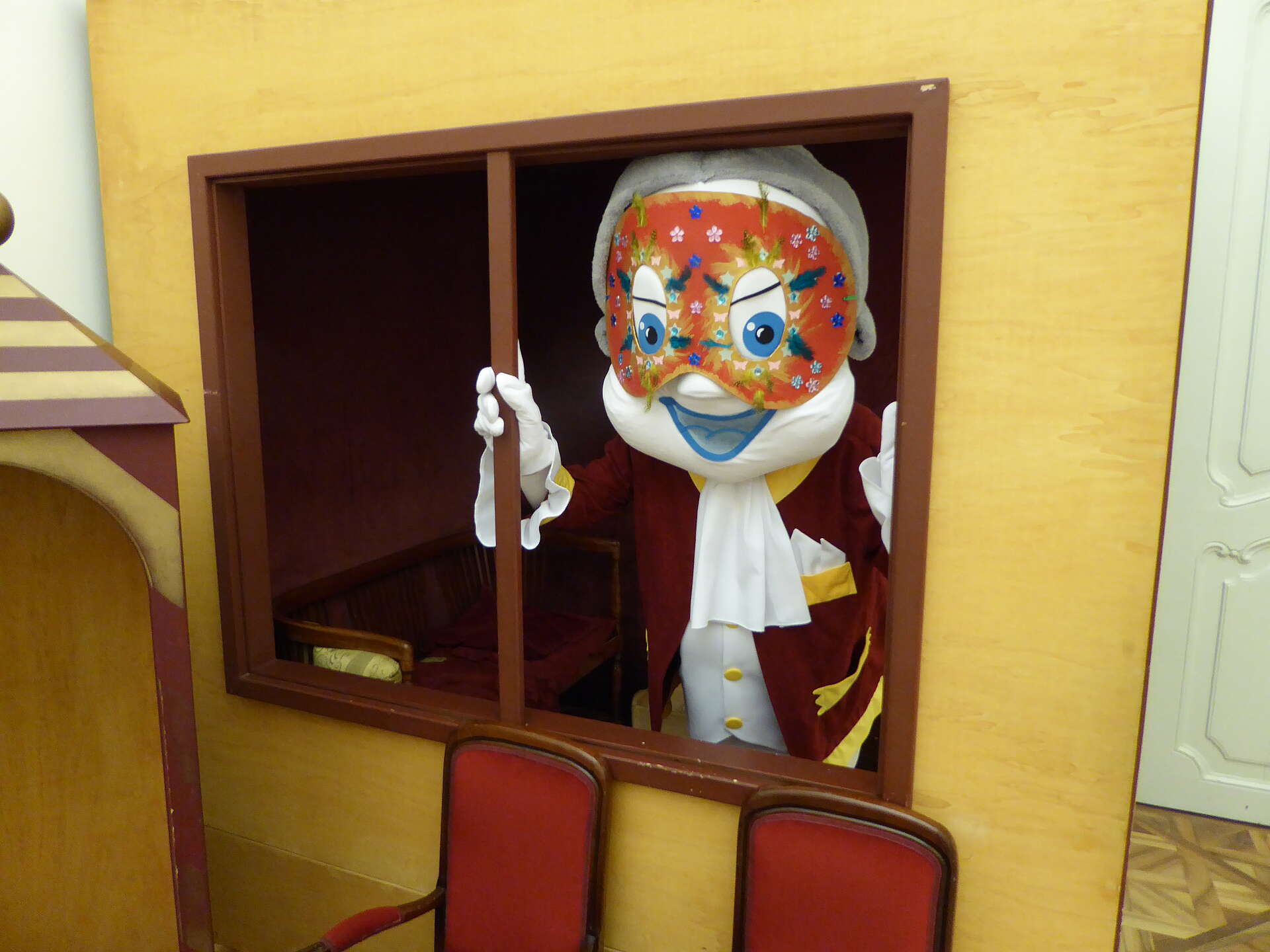 Poldi trägt eine Faschingsmaske und blickt durch einen Rahmen im Kindermuseum Schloss Schönbrunn