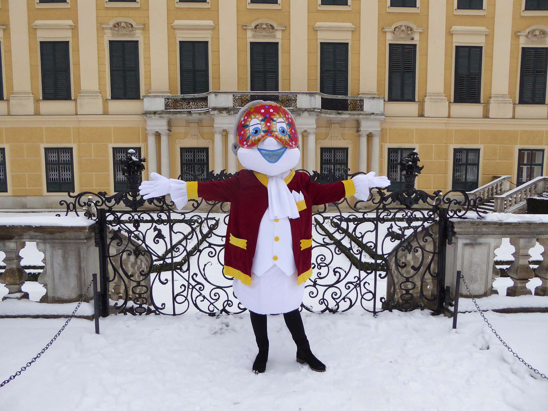 Poldi trägt einen Faschingsmaske und steht im schneebedeckten Schlosspark Schönbrunn