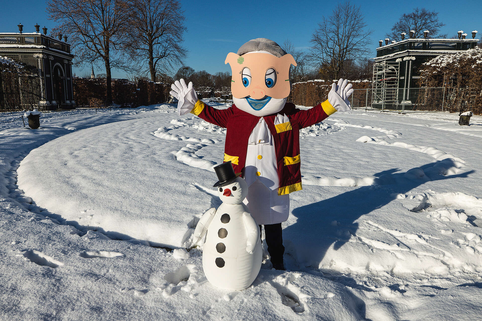 Schlossgeist Poldi steht im Schnee, trägt eine Faschingsmaske und baut einen Schneemann