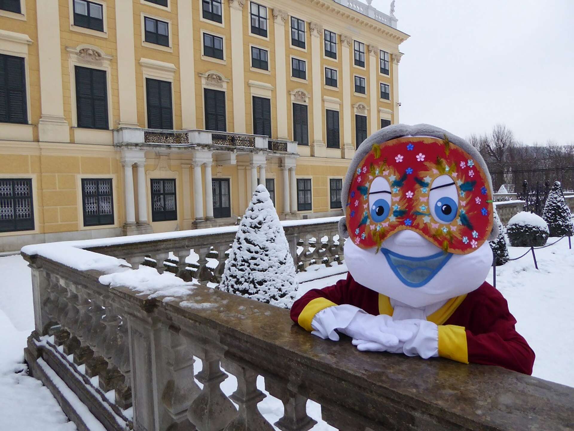 Poldi trägt einen Faschingsmaske und steht im schneebedeckten Schlosspark Schönbrunn
