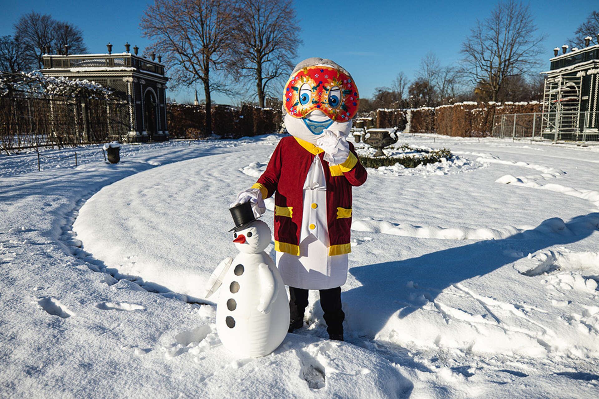 Poldi trägt eine Faschingsmaske und steht im Schnee, vor ihm ein Schneemann